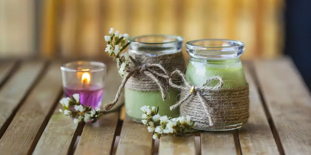 Two candle jars with wick tied around them on a wooden table.