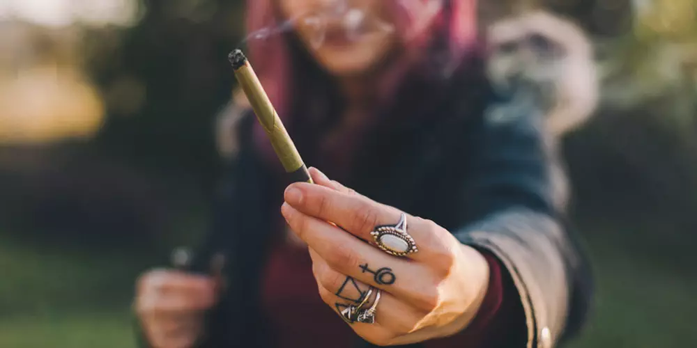 girl holding a lit blunt out in focus of the camera