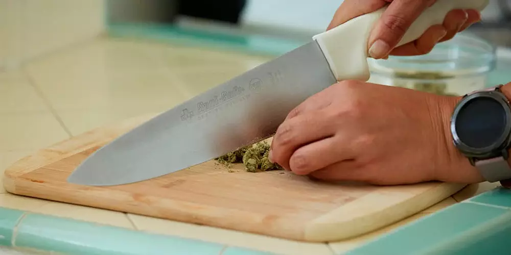 A person is slicing a piece of marijuana on a cutting board.