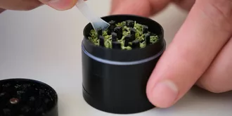 two hands using plastic scraper to clean marijuana grinder
