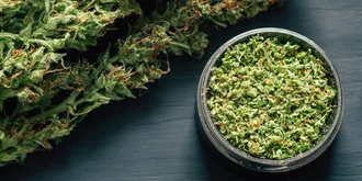 A bowl of cannabis leaves on a dark table.